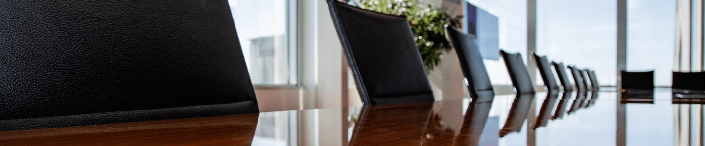 A closeup of the boardroom with a brown desk and black leather chairs.