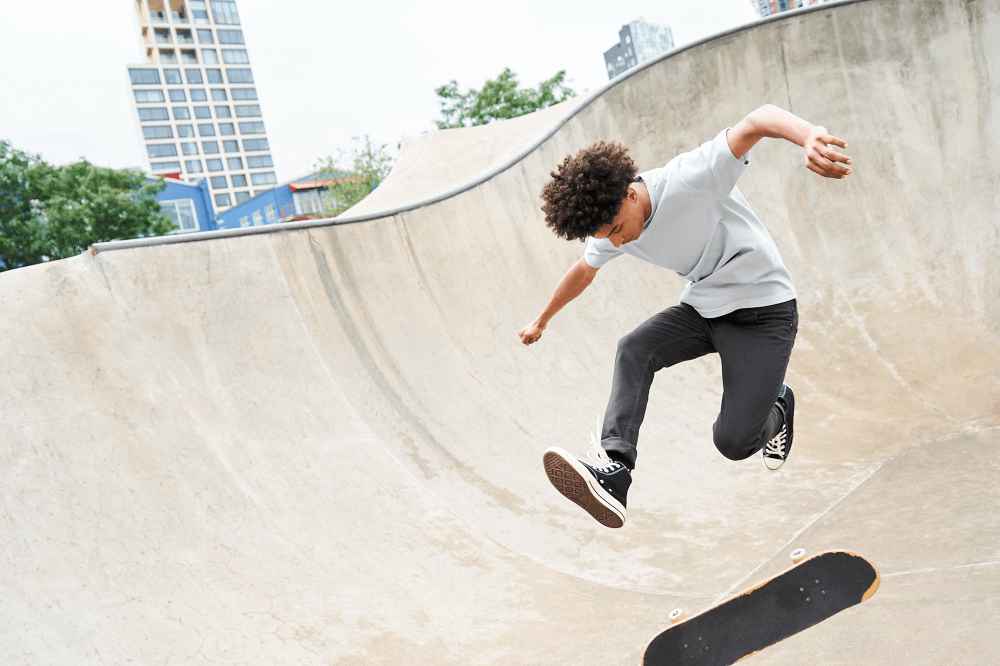 A man wearing a blue t-shirt is jumping off a skateboard at a skatepark.