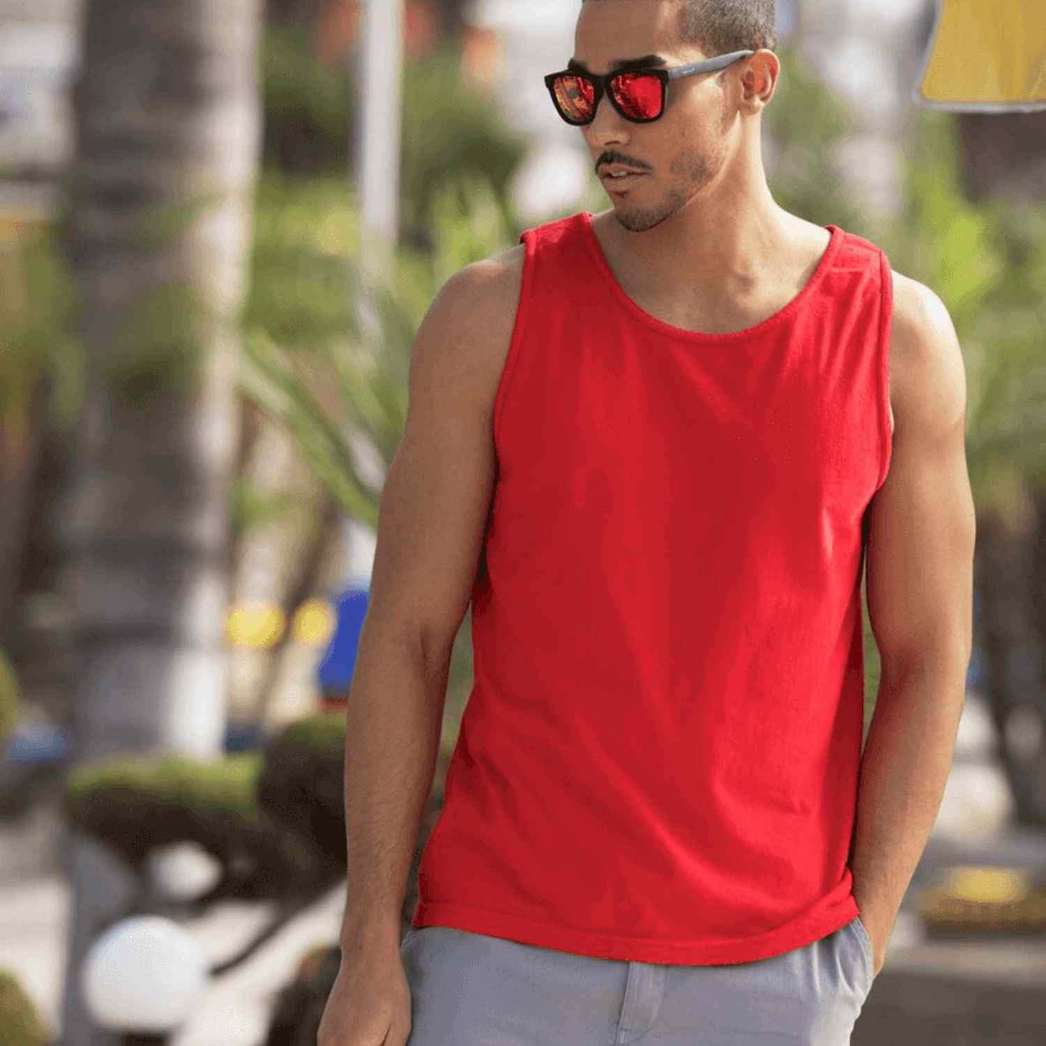 Un homme en lunettes de soleil porte un débardeur rouge et regarde au loin.