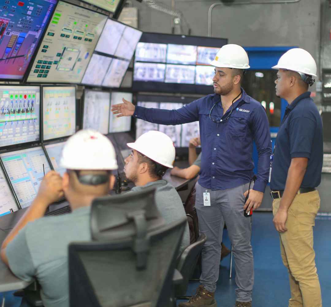 Employees wearing hard hats are looking at computer screens.