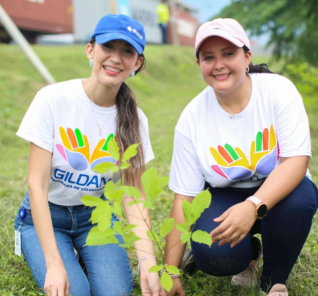 2 employees kneeling outside on the grass next to the tree sapling they planted together.
