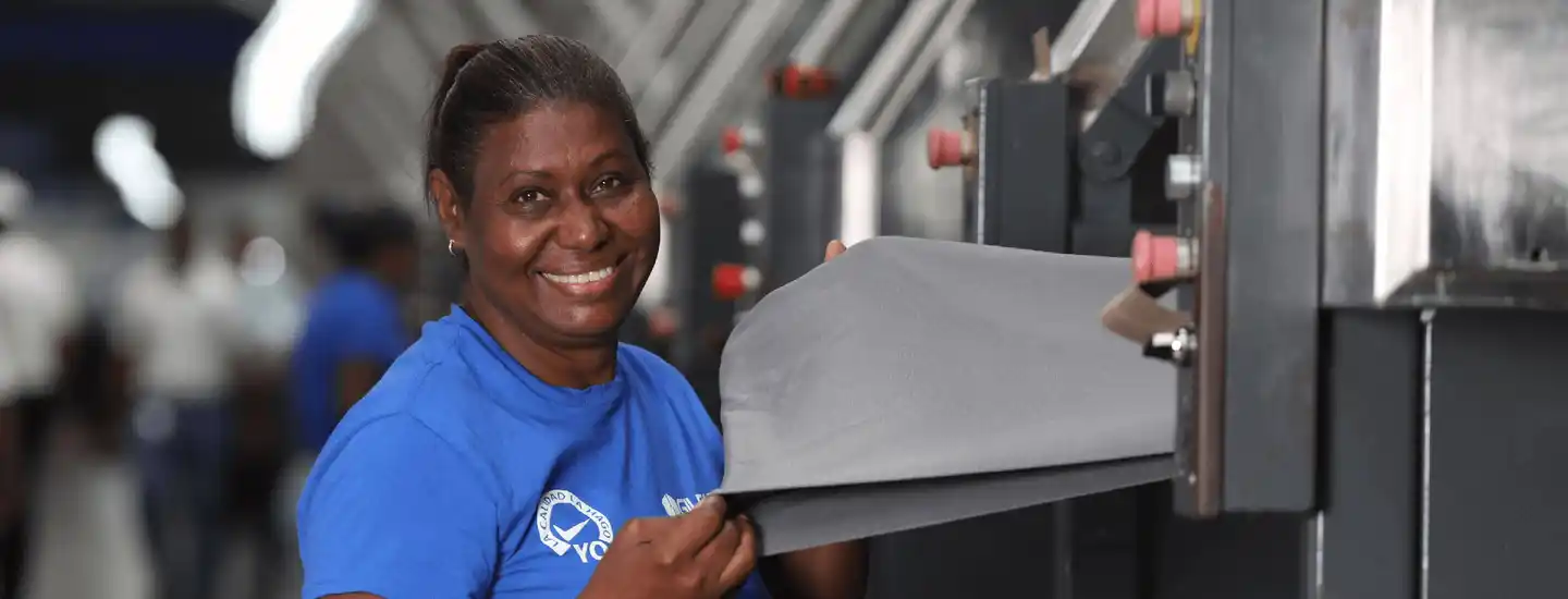 Une employée portant une chemise bleue Gildan tient un morceau de tissu et sourit.