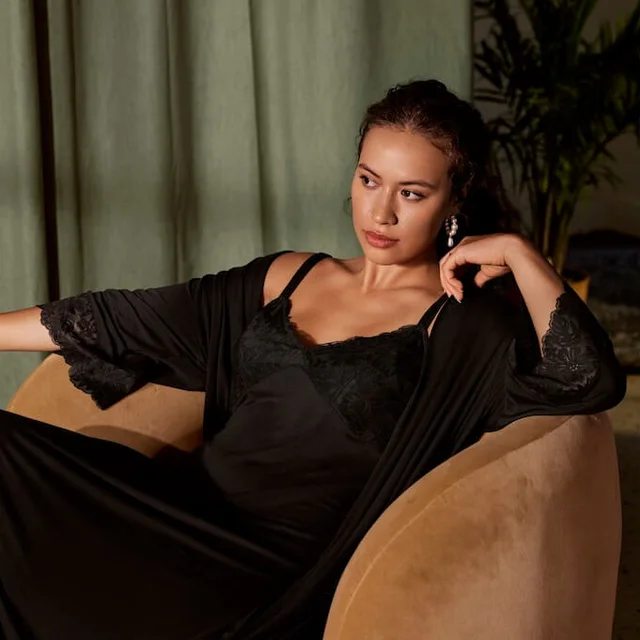 A woman sitting on a chair looking away from the camera wearing black sleepwear.