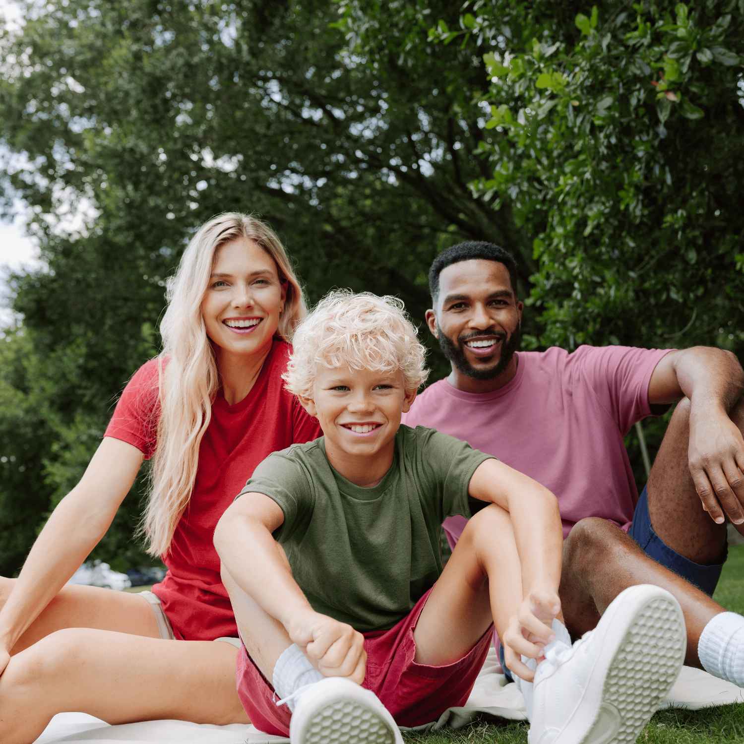 A woman, man, and boy are sitting outside on the grass smiling.