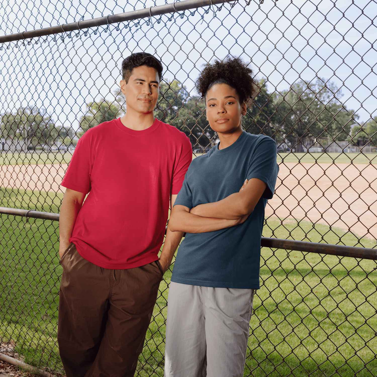 A woman and man are outside wearing Gildan t-shirts leaning against a fence.