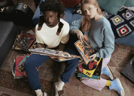 A man and woman are sitting on the floor looking up at the camera holding vinyl records.
