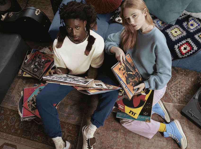 A man and woman are sitting on the floor looking up at the camera holding vinyl records.