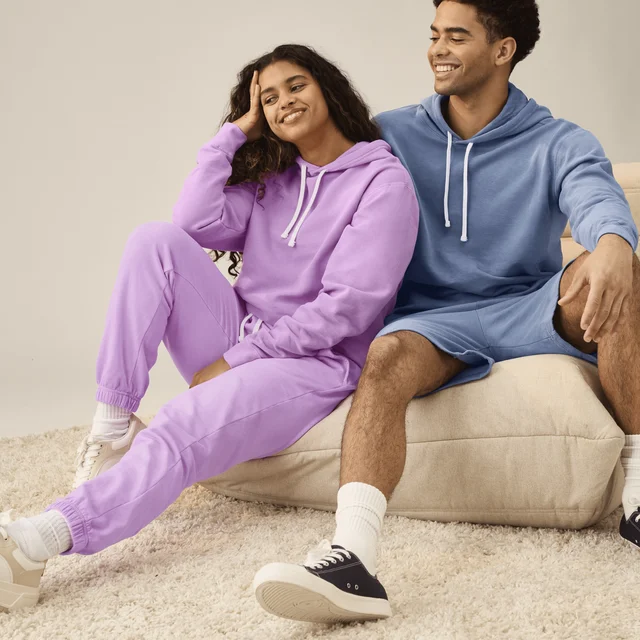 A woman and man wearing a purple and blue Comfort Colors tracksuit smiling on a couch.