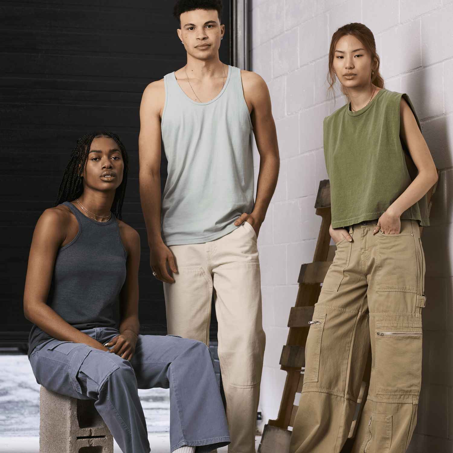 Two women and a man are wearing American Apparel tank tops looking into the camera in an industrial setting.