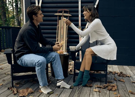 A woman laughing sitting outside on a chair wearing blue GOLDTOE socks.