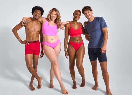 A woman wearing purple and a man wearing pink are sitting on the floor leaning against each other.