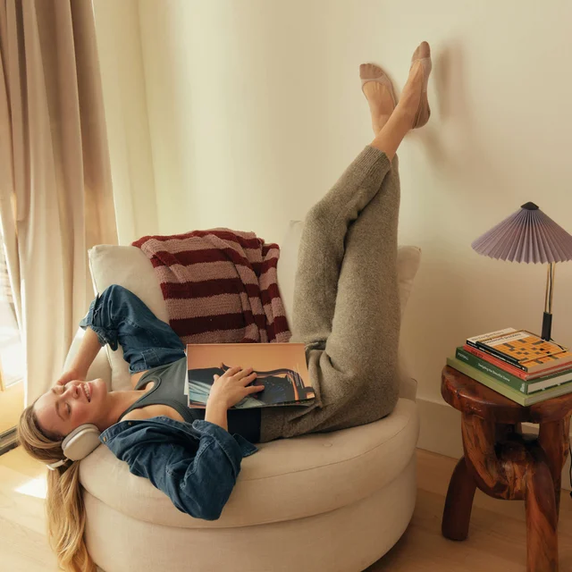 Una mujer tumbada en una silla escuchando música con los pies en el aire llevando calcetines Peds no show.
