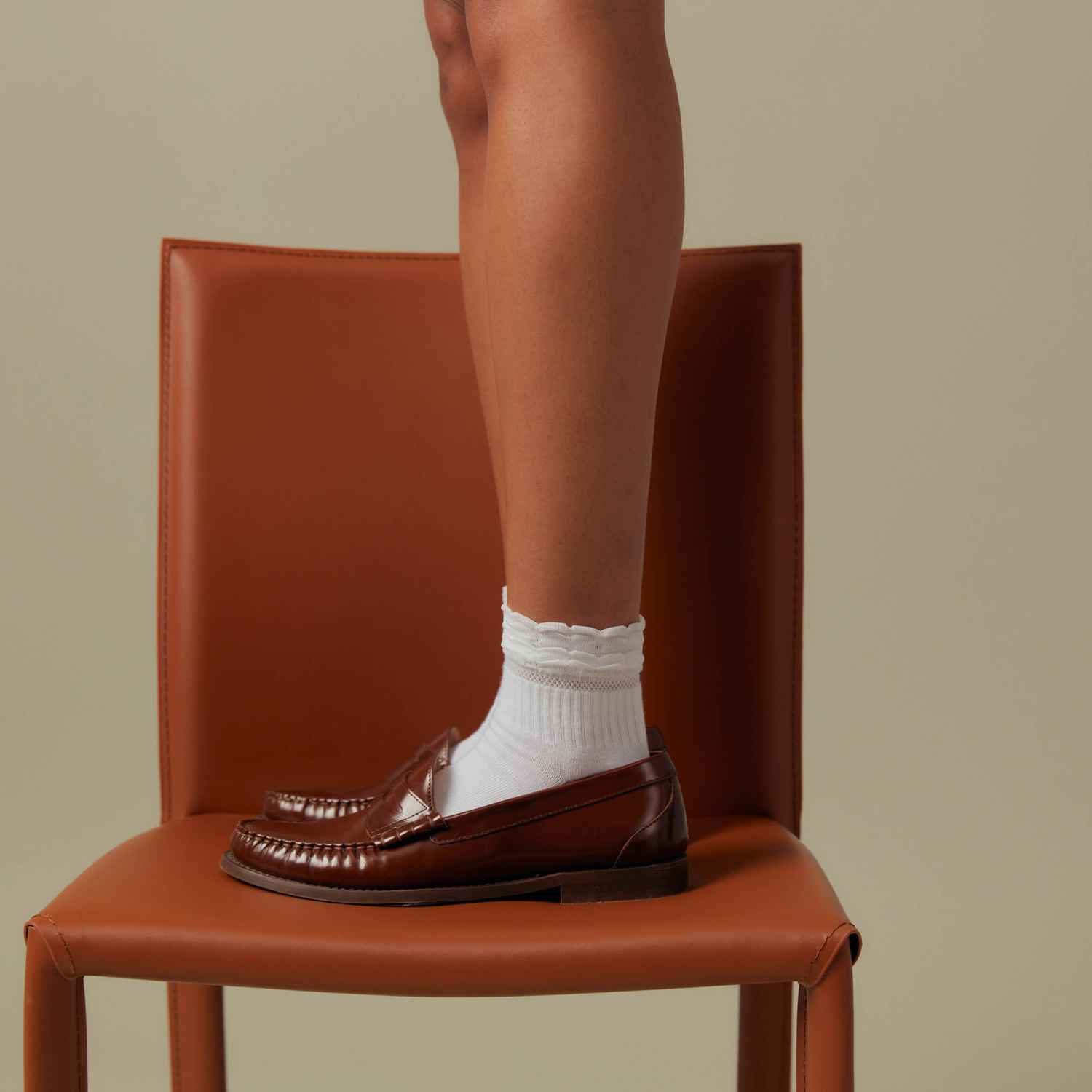 A woman is standing on a brown leather chair wearing white Peds socks.