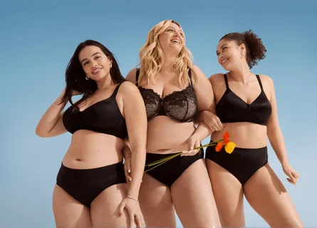 A woman wearing purple and a man wearing pink are sitting on the floor leaning against each other.