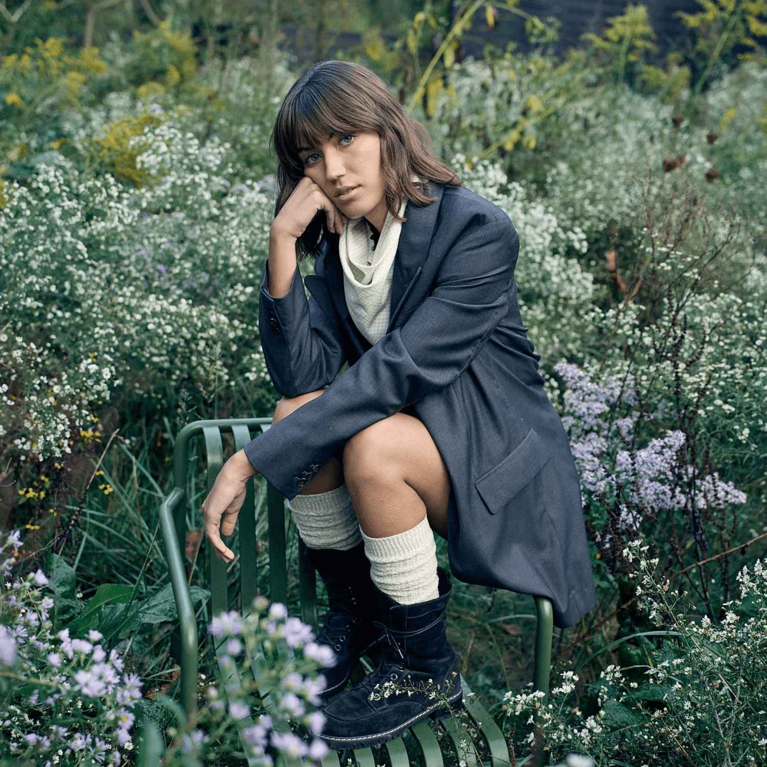 A woman is sitting on a chair in a field of flowers wearing white GOLDTOE high rise socks.