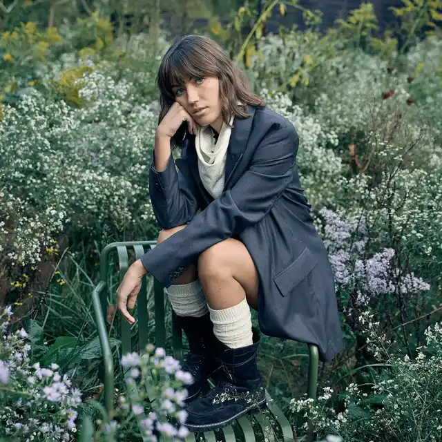 A woman is sitting on a chair in a field of flowers wearing white GOLDTOE high rise socks.