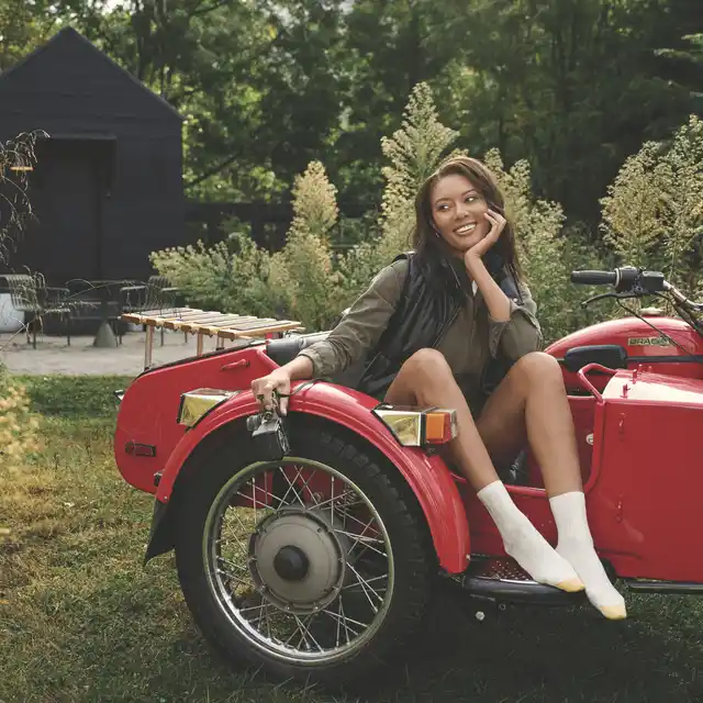 A woman sitting in a red car outside in wearing white GOLDTOE socks with a gold tip.