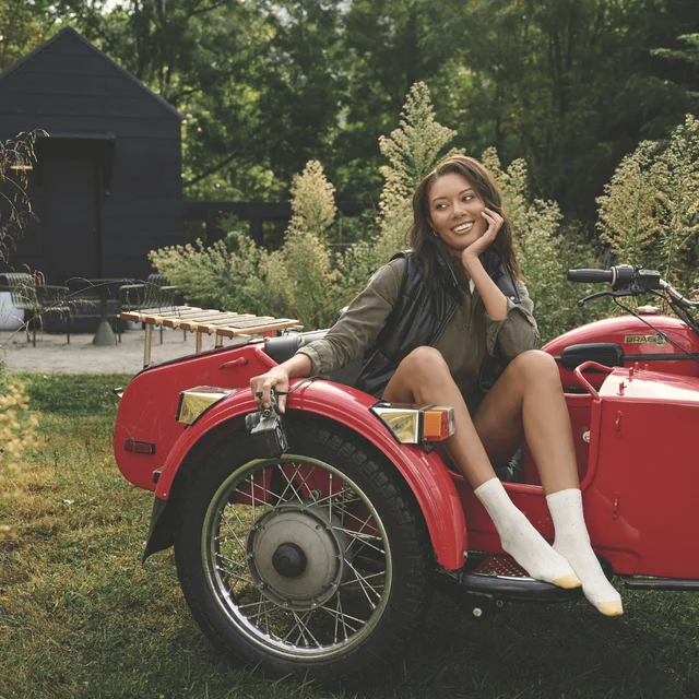 A woman sitting in a red car outside in wearing white GOLDTOE socks with a gold tip.