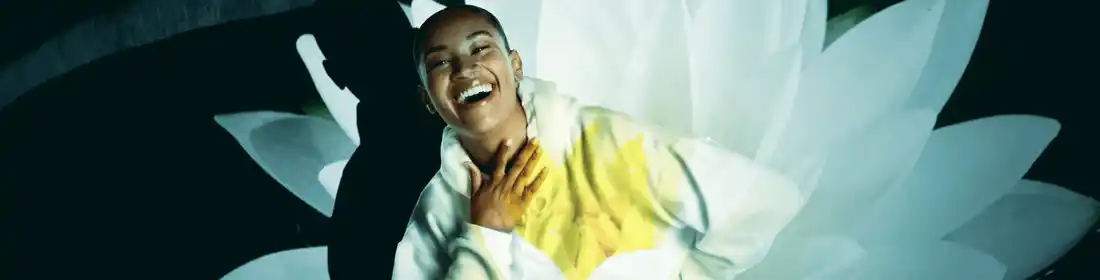 Femme en pull blanc riant avec une fleur en surimpression.