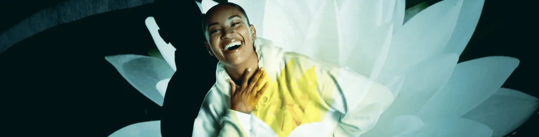 Femme en pull blanc riant avec une fleur en surimpression.