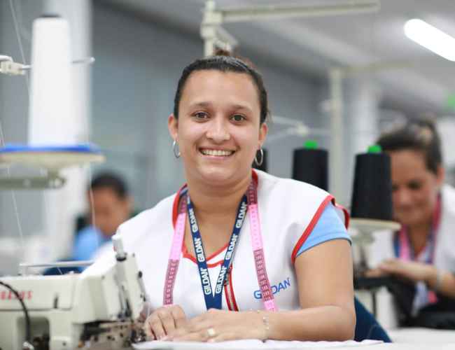 A female sewing operator at Gildan is smiling at the camera.
