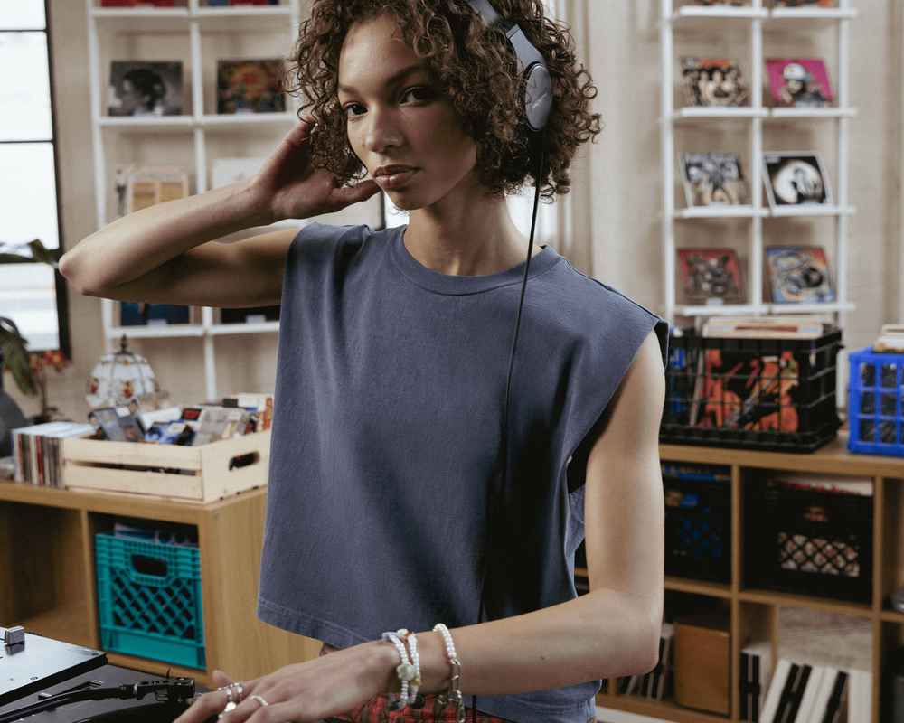 A woman is wearing a grey American Apparel tank top and headphones.