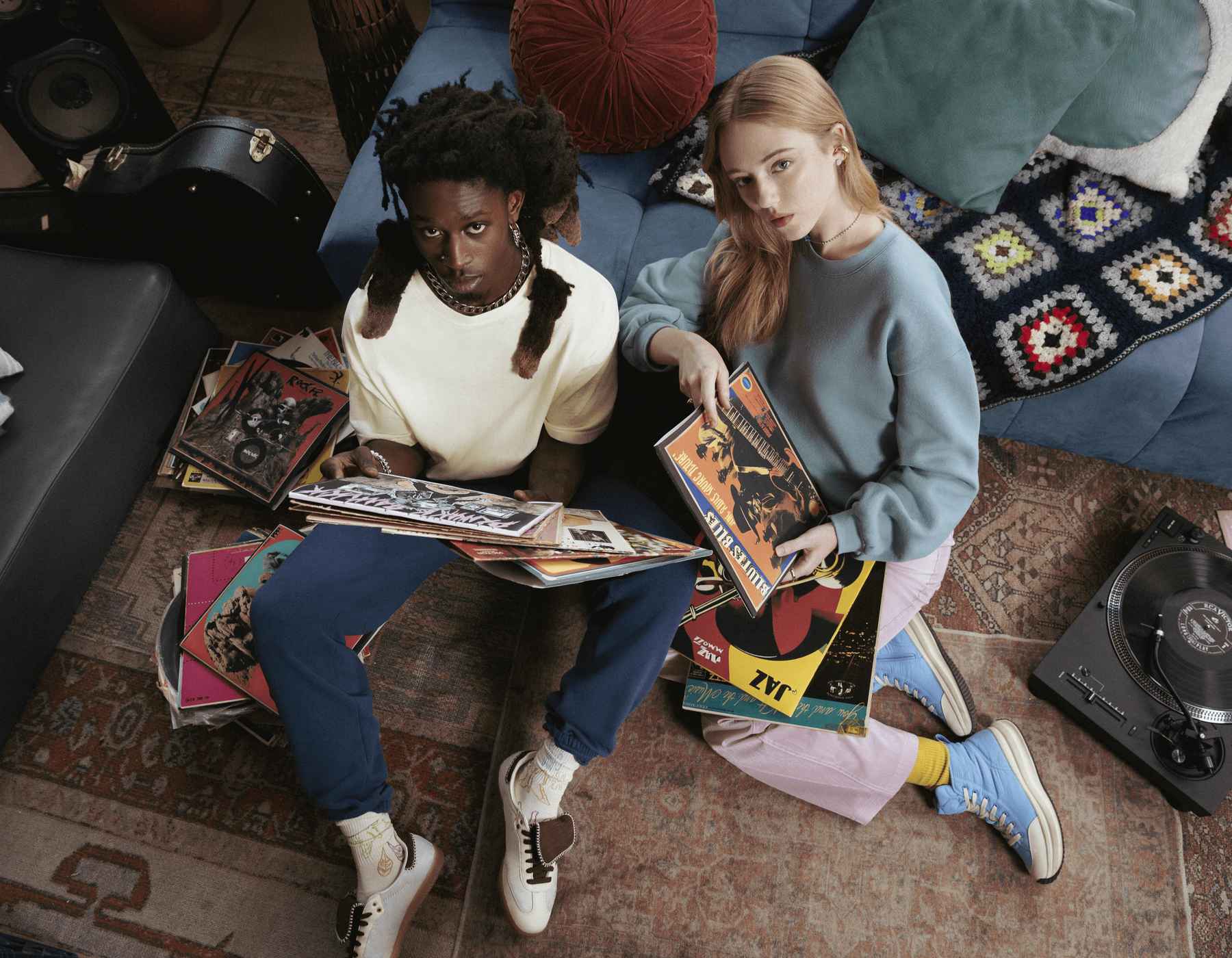 A man and woman are sitting on the floor looking up at the camera holding vinyl records.