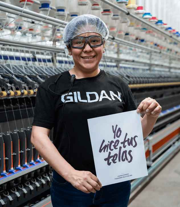 Antonia is smiling at the camera and holding a sign that reads “I made your fabric” in Spanish.
