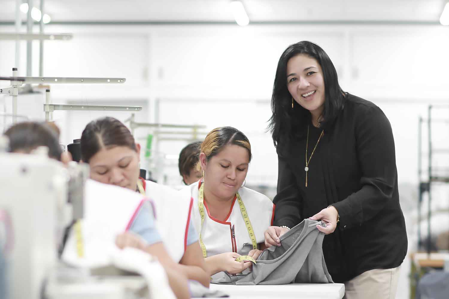 A manager is smiling at the camera while helping a sewing employee.