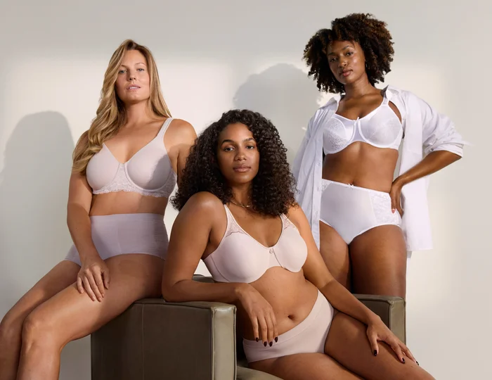 3 women sitting on a chair wearing white undergarments.