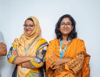 Two women from Bangladesh are smiling at the camera and crossing their arms.