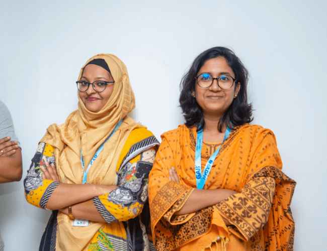 Deux femmes du Bangladesh sourient à la caméra et croisent les bras.