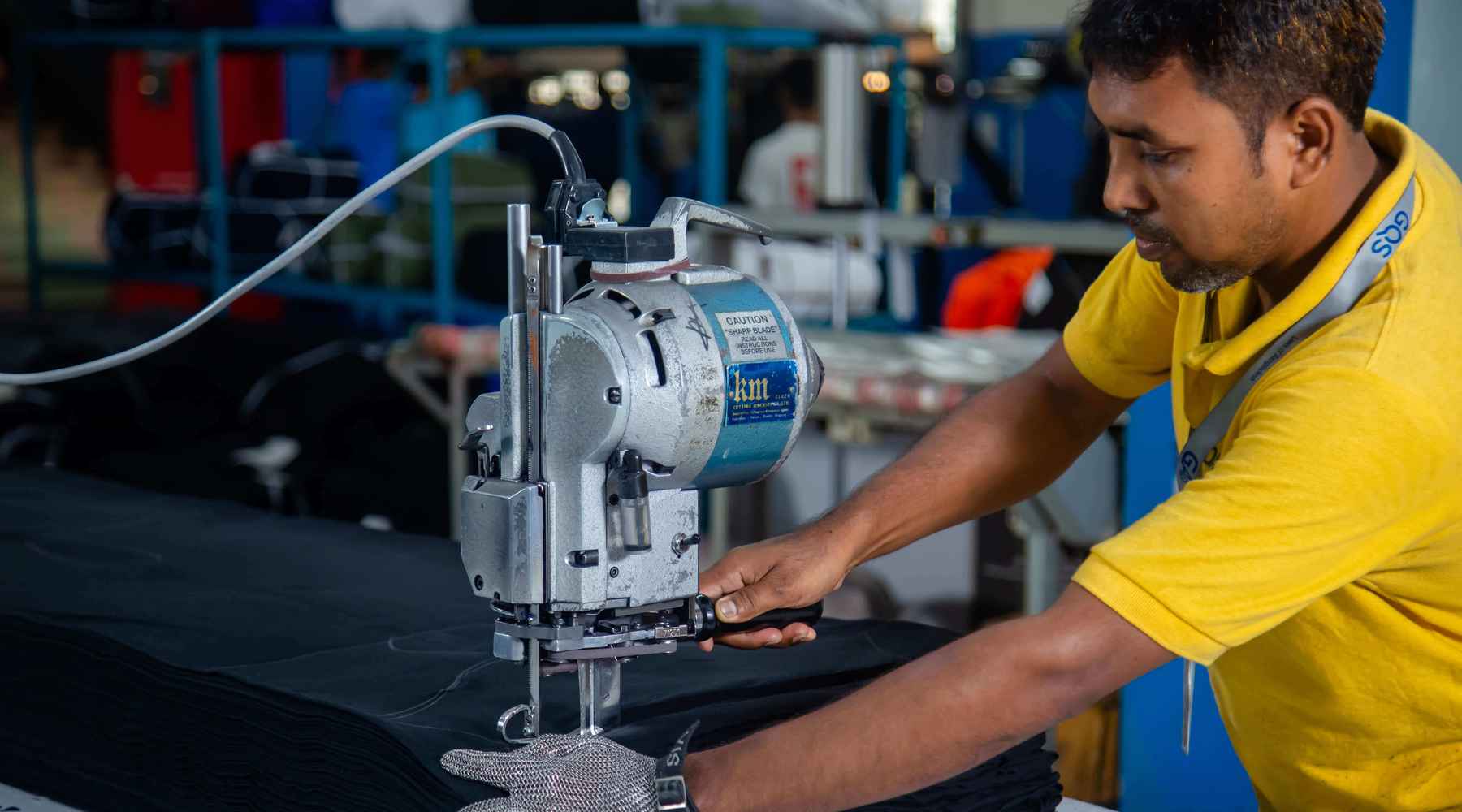 A man in a yellow shirt is operating a fabric cutting machine.