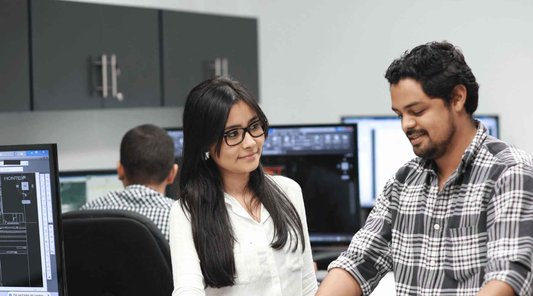 Two employees in Nicaragua are standing in front of a desk next to a computer.