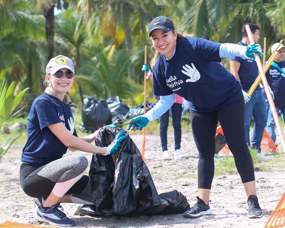 Two female employees are helping to clean the beach in Honduras and smiling.