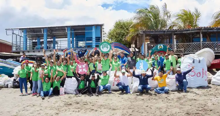 Un gran grupo de empleados en Nicaragua sonríen en la playa con las manos en alto.