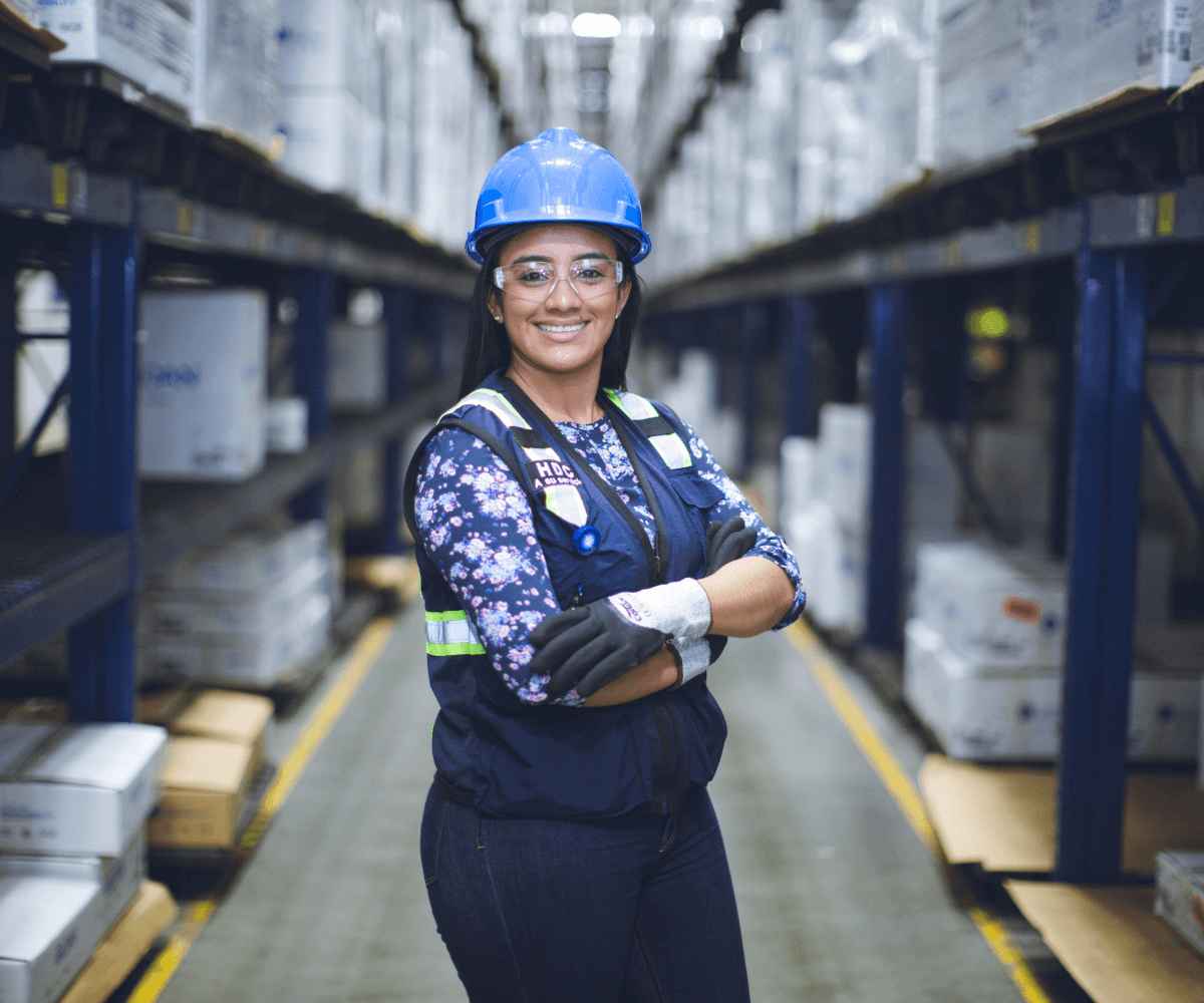 A woman wearing a safety vest and hard hat is smiling in the distribution center.