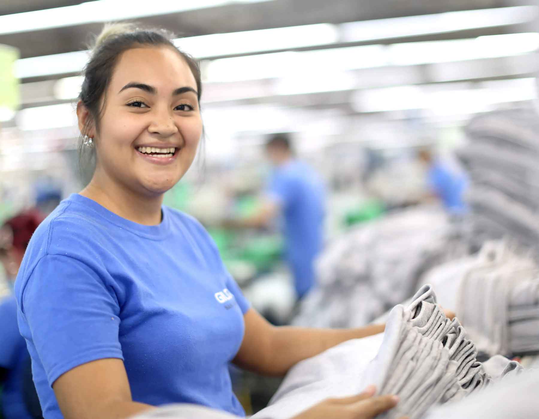 A Gildan sewing employee is smiling at the camera.