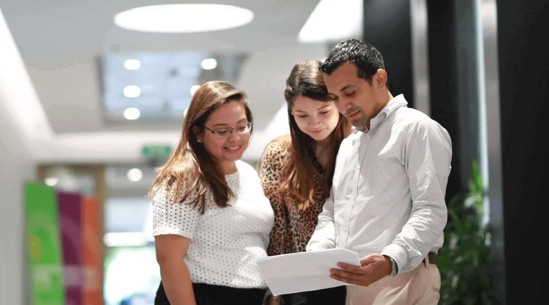 Tres empleados de Honduras están de pie en el pasillo y conversan mirando un papel.