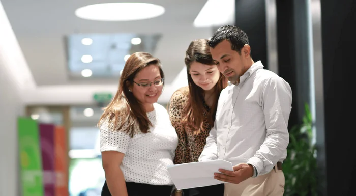 Three employees in Honduras are standing in the hallway and looking at a paper in conversation.