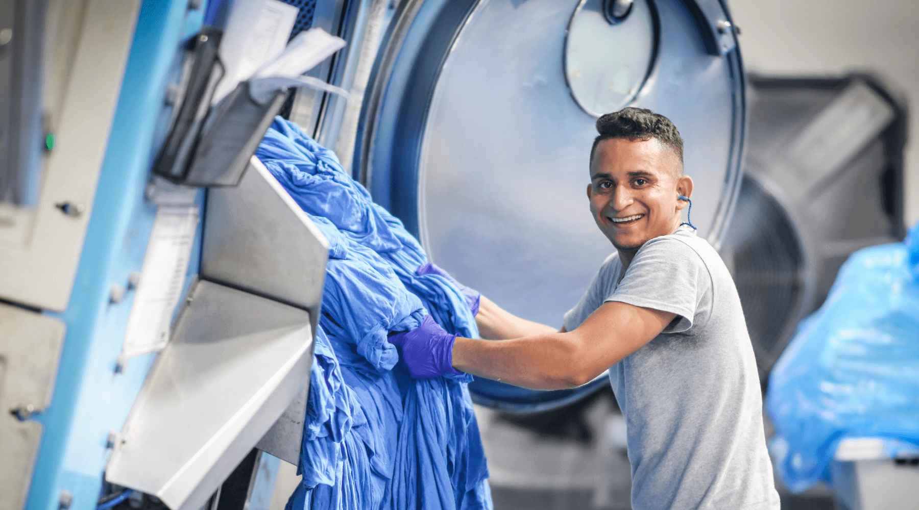 A man is taking wet Gildan blue fabric out of a jet machine.