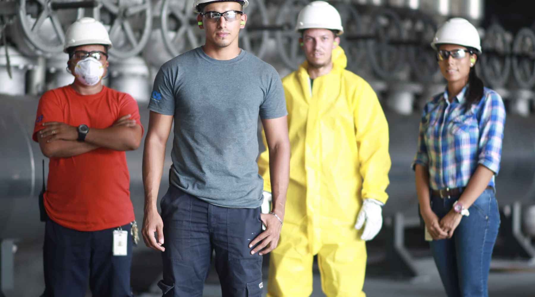 Four employees are wearing white hard hats and safety goggles, looking at the camera.
