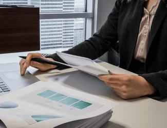 A woman is on a laptop while looking through papers of a Gildan report.