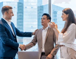 Three employees in Singapore are in a high-rise office shaking hands and smiling.