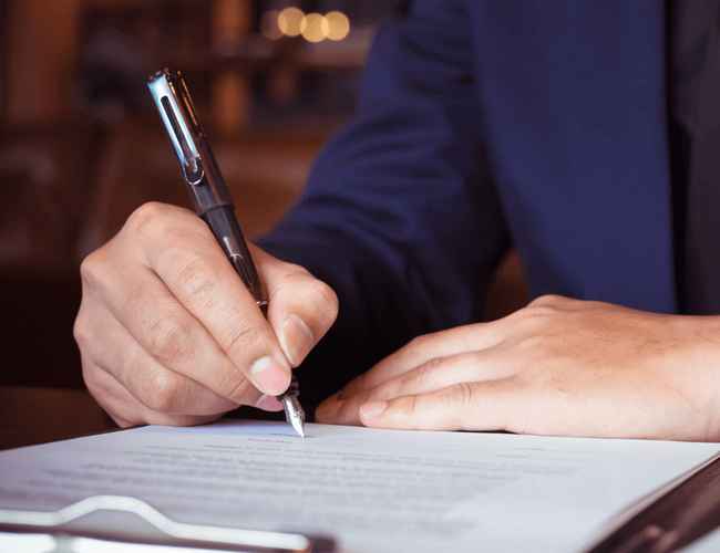 Un hombre está escribiendo en un papel con una pluma estilográfica.