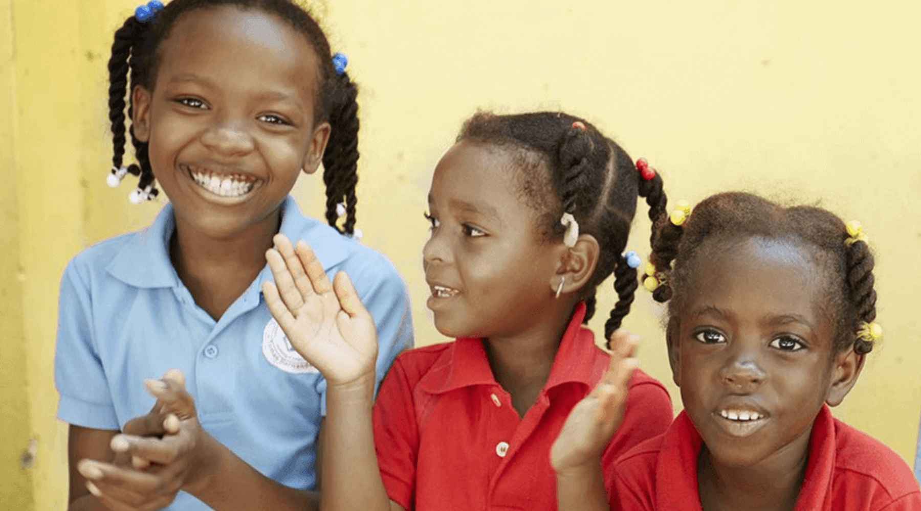 Tres niños de la República Dominicana sonríen y aplauden.