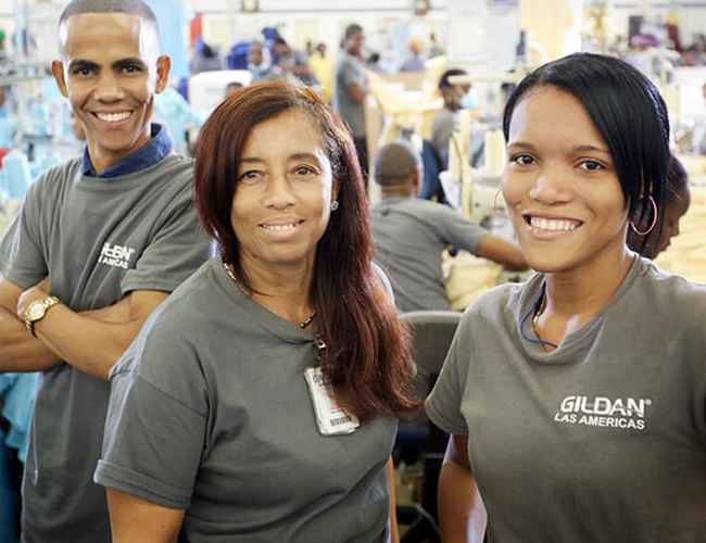 Three Gildan sewing employees from Las Americas, Dominican Republic, are smiling at the camera.