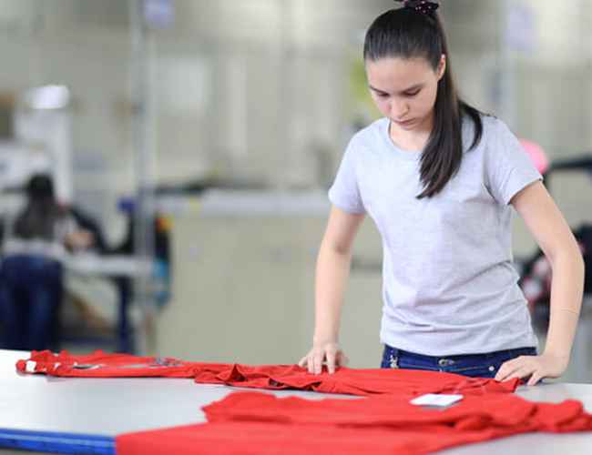 Un trabajador de control de calidad de Gildan revisando una camisa roja.