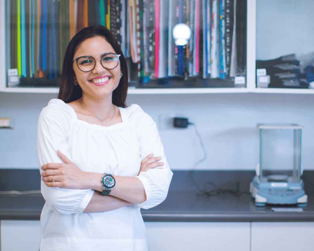 A female employee is standing next to a selection of multi-colored Gildan fabrics and smiling.