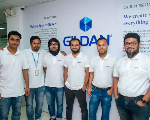 A group of employees from Bangladesh are standing next to a wall with Gildan signage on it.